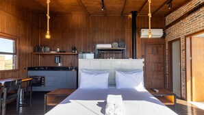 Una habitación con cama, una mesa de madera, zona de cocina y pared de ladrillo.