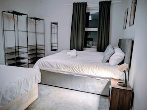 A bedroom with a bed, a wooden nightstand, a mirror, a black metal shelving unit, and a window with curtains. - 4 The Croft (Hexham)