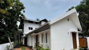 Une maison moderne à deux étages, avec une façade blanche, un toit en pente et un petit porche à l’avant.