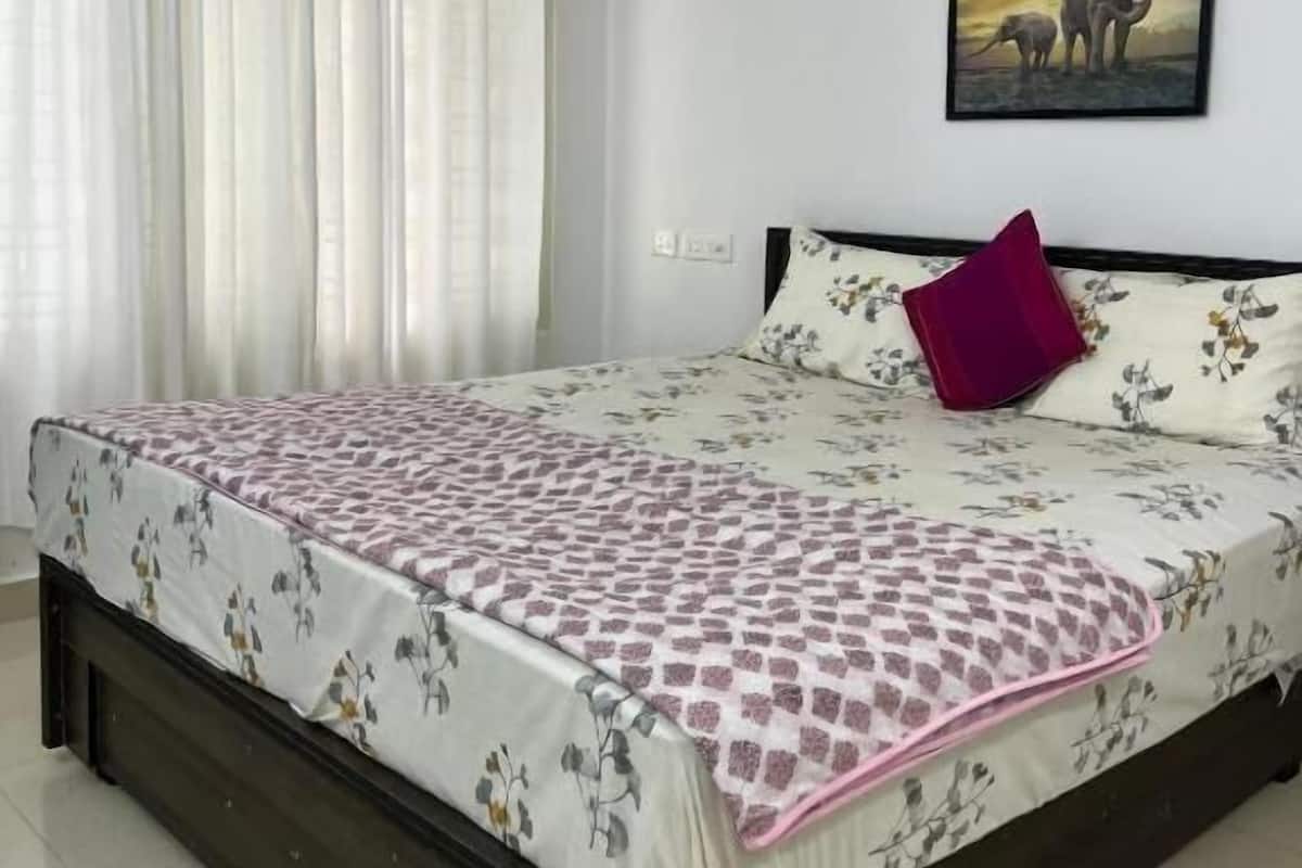 A bedroom with a bed, white curtains, a painting of elephants, and a window.