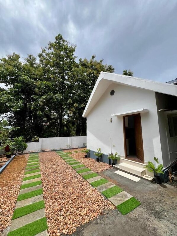 A modern house with a white exterior, a small porch, and a pathway leading to the entrance. - Little Chandhana Guest House (Kottayam)