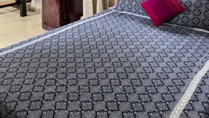 Une chambre avec une couvre-lit à motifs, un escalier en bois, une fenêtre donnant sur des palmiers et un coussin rouge.