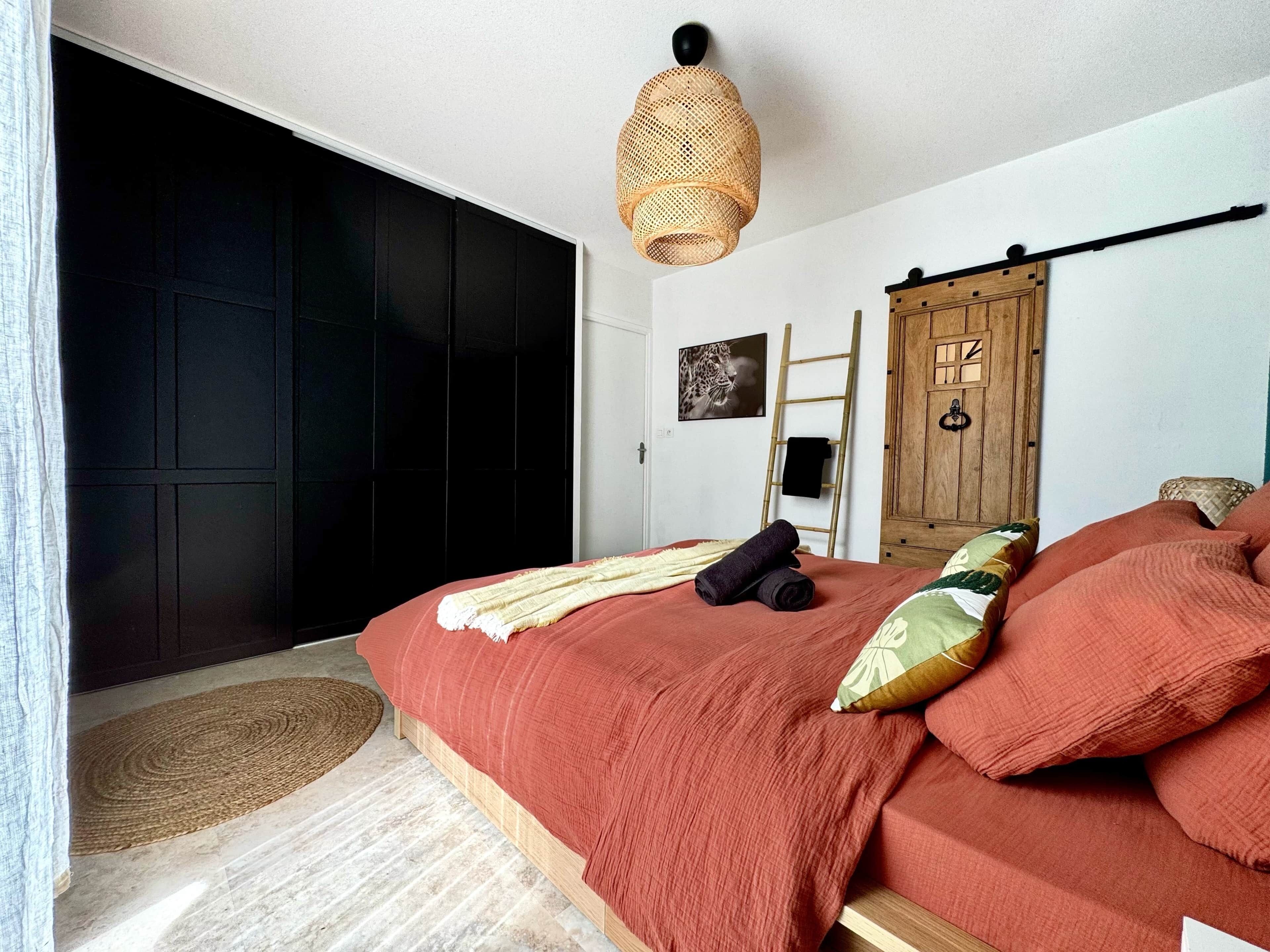 Ein Schlafzimmer mit einem großen Bett, einem Holzschrank, einer Leiter und einer gewobenen Lampe.