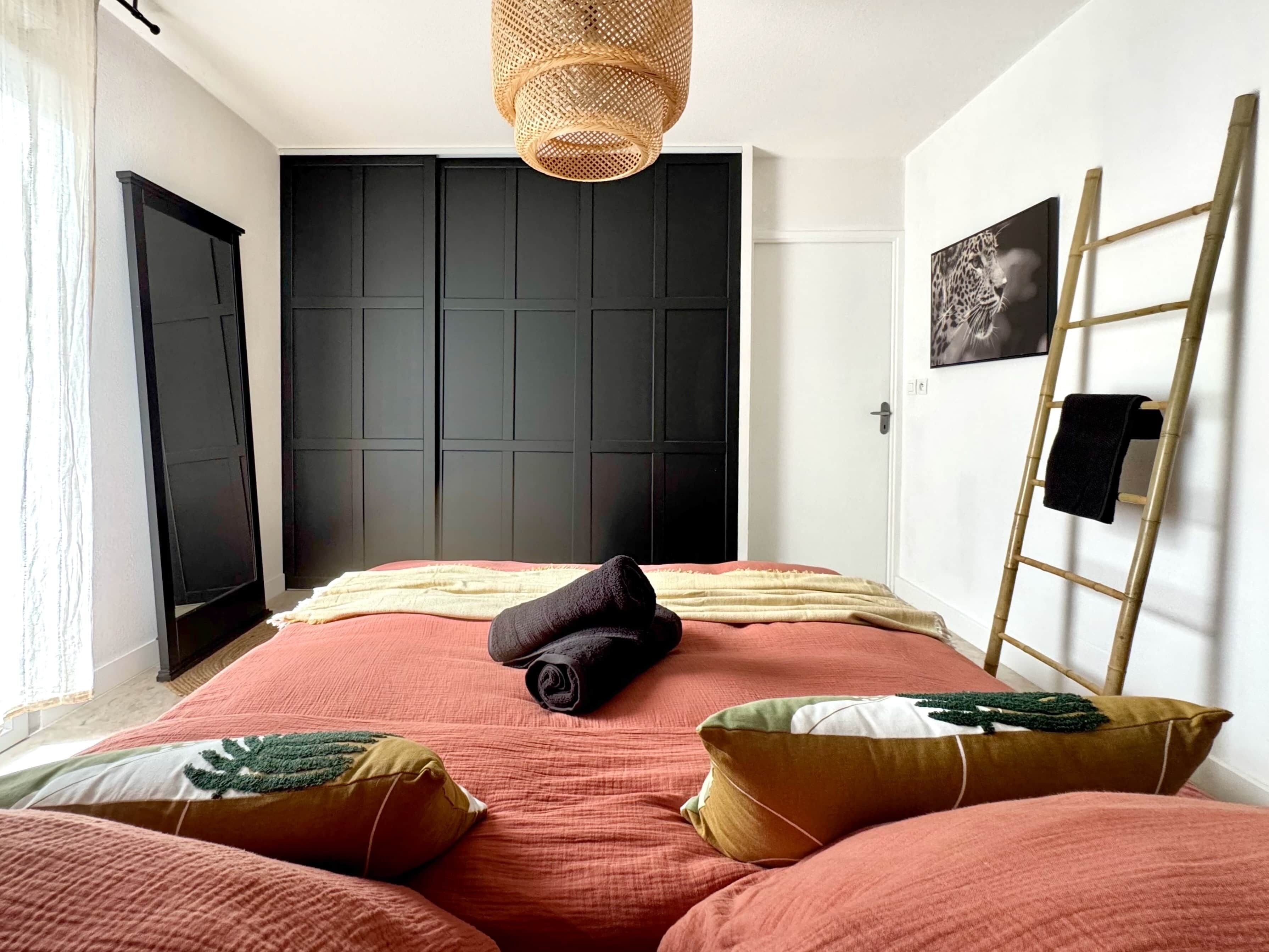 Ein Schlafzimmer mit Bett, Kissen, Decke, einer Hängeleuchte, einer Leiter und einer Tür.