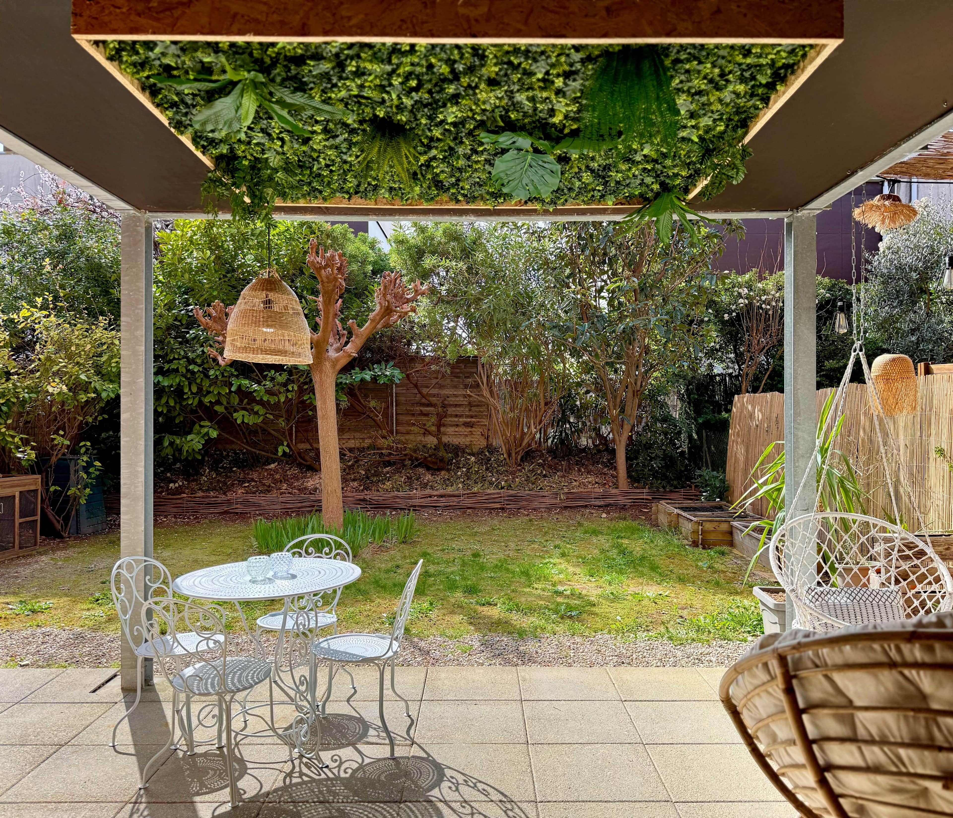 Un espacio de patio cubierto con una mesa y sillas, una cesta colgante y vistas al jardín.