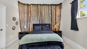Un dormitorio con cama, mesitas de noche, ventana y cortinas.