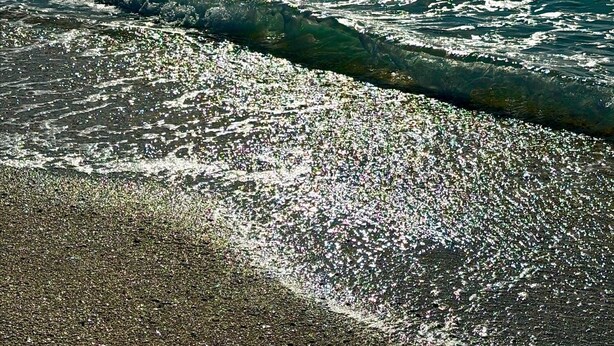 Una playa con el sol reflejándose en el agua y un cielo despejado.