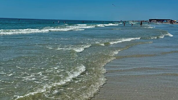 A beach with clear water, waves, and people. - Spacious • Walk to Beach • Pool & Lake Padre Views • Fishing Dock [6 night min.] (Corpus Christi)