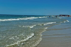 A beach with clear water, waves, and people. - Spacious • Walk to Beach • Pool & Lake Padre Views • Fishing Dock [6 night min.] (Corpus Christi)