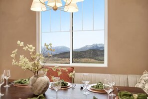 Une table à manger dressée pour un repas, avec vue sur les montagnes par la fenêtre.