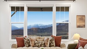 A living room with a sofa and armchairs, a coffee table, and a view of mountains through large windows. - Deer Valley Basecamp with Hot Tub and Views (Heber City)