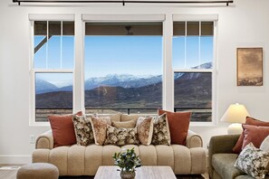 Ein Wohnzimmer mit einer Couch und Sesseln, einem Couchtisch und Blick auf Berge durch große Fenster.