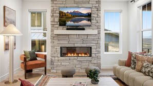 A living room with a stone fireplace, a flat-screen TV mounted above it, and a cozy seating area with a sofa and armchairs. - Deer Valley Basecamp with Hot Tub and Views (Heber City)
