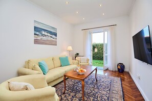Ein Wohnzimmer mit einer Couch, einem Couchtisch, einem Fernseher und Blick ins Freie.