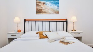 A bed with white bedding, a wooden headboard, two bedside tables with lamps, and a painting of a beach scene above the bed. - Green Horizon - One Bedroom Apartment, Sleeps 4 (Dubrovnik)