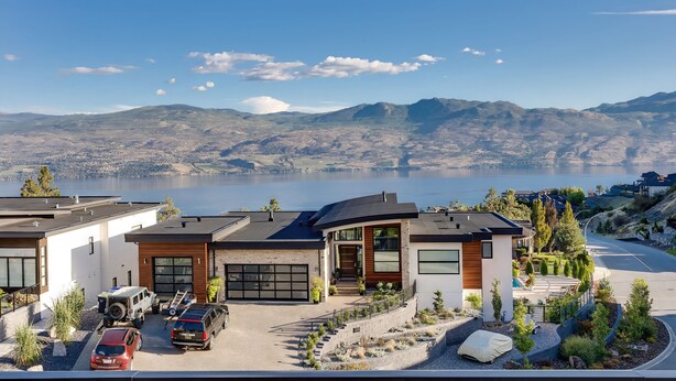 Een modern huis met een garage, oprit en uitzicht op een meer en bergen.