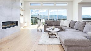 Een moderne woonkamer met een grote hoekbank, een open haard en uitzicht op bergen door grote ramen.