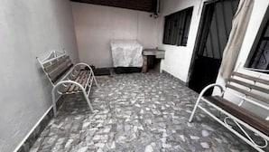 A small room with a tiled floor, a bench, a table with a white cloth, and a window with a curtain.
