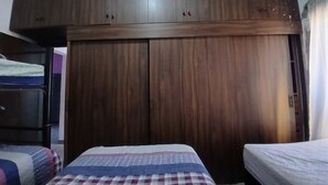 A bedroom with a large wooden wardrobe, a bed with a checkered bedspread, and a bedside table.