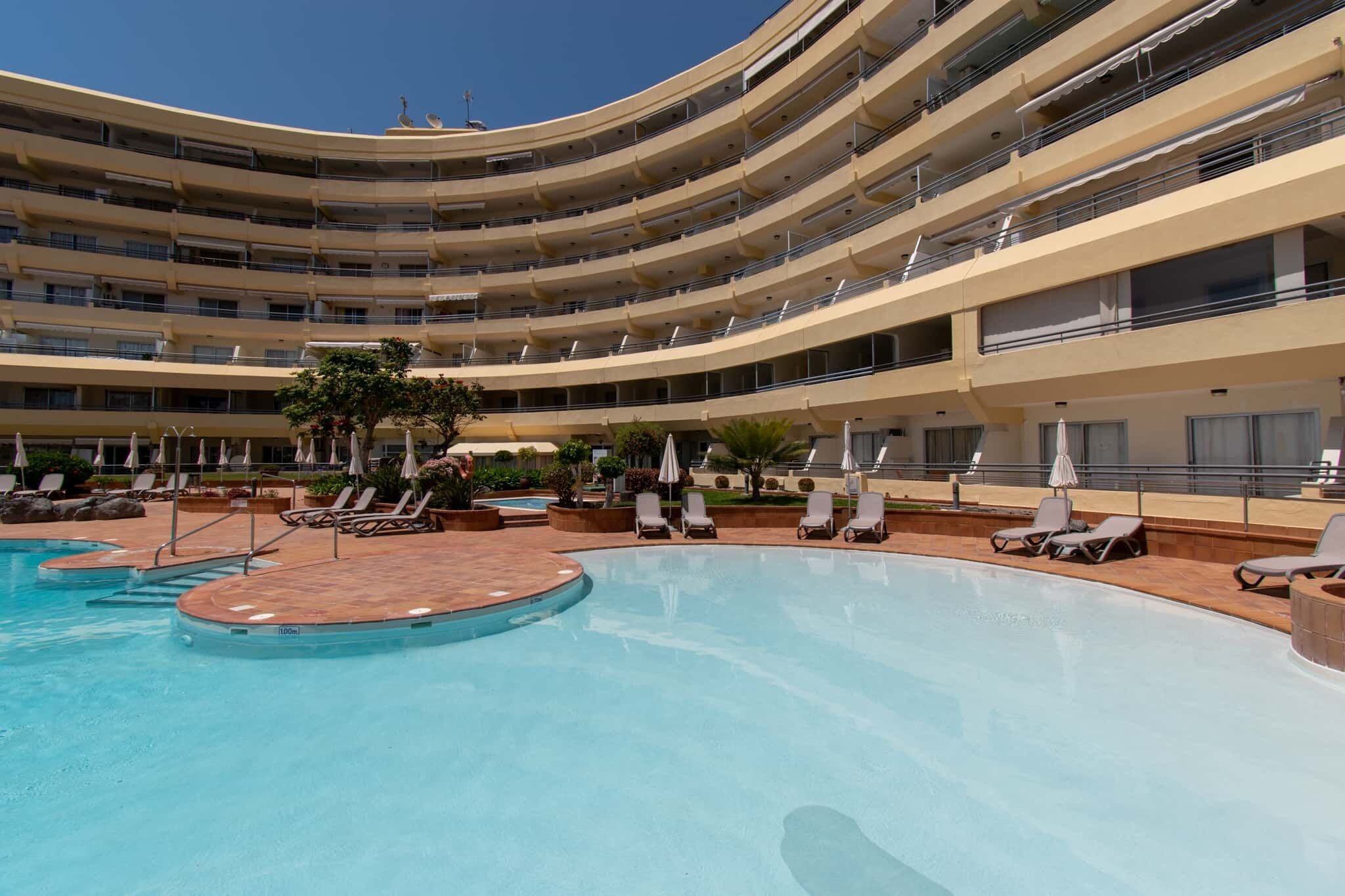 A multi-story hotel with a central swimming pool surrounded by sun loungers and umbrellas.