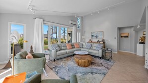 Een moderne woonkamer met een hoekbank, een ronde salontafel en een groot raam met uitzicht op de omgeving.