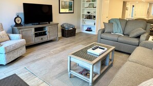 Ein Wohnzimmer mit einer Couch, einem Couchtisch, einem Fernseher und einem Bücherregal.