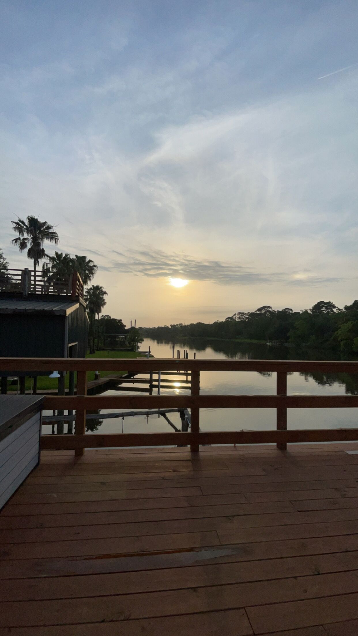 A wooden deck overlooking a calm body of water with a sunset in the background.