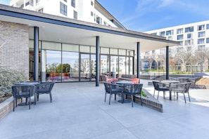 Un espace extérieur aménagé en terrasse, avec des tables et des chaises, un coin salon abrité et une vue sur les bâtiments environnants.