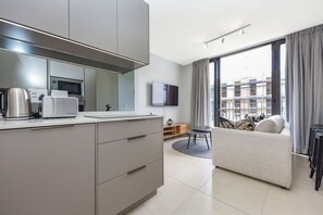 Eine moderne Küche mit Mikrowelle, Wasserkocher und Toaster. Im Wohnbereich befindet sich eine Couch und ein Esstisch.