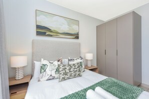 Ein ordentlich eingerichtetes Schlafzimmer mit einem Bett, zwei Nachttischen, einem Beistelltisch, einer grünen Tagesdecke und einem großen Kleiderschrank.