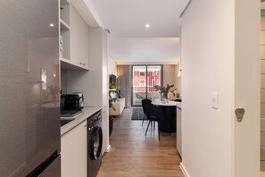 Una cocina moderna con lavadora incorporada, un comedor con mesa y sillas, y vistas al exterior a través de un ventanal.