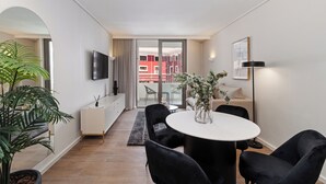Ein modernes Wohnzimmer mit einem runden Tisch, schwarzen Stühlen, einem Fernseher und einem Balkon mit roten Gebäuden im Hintergrund.