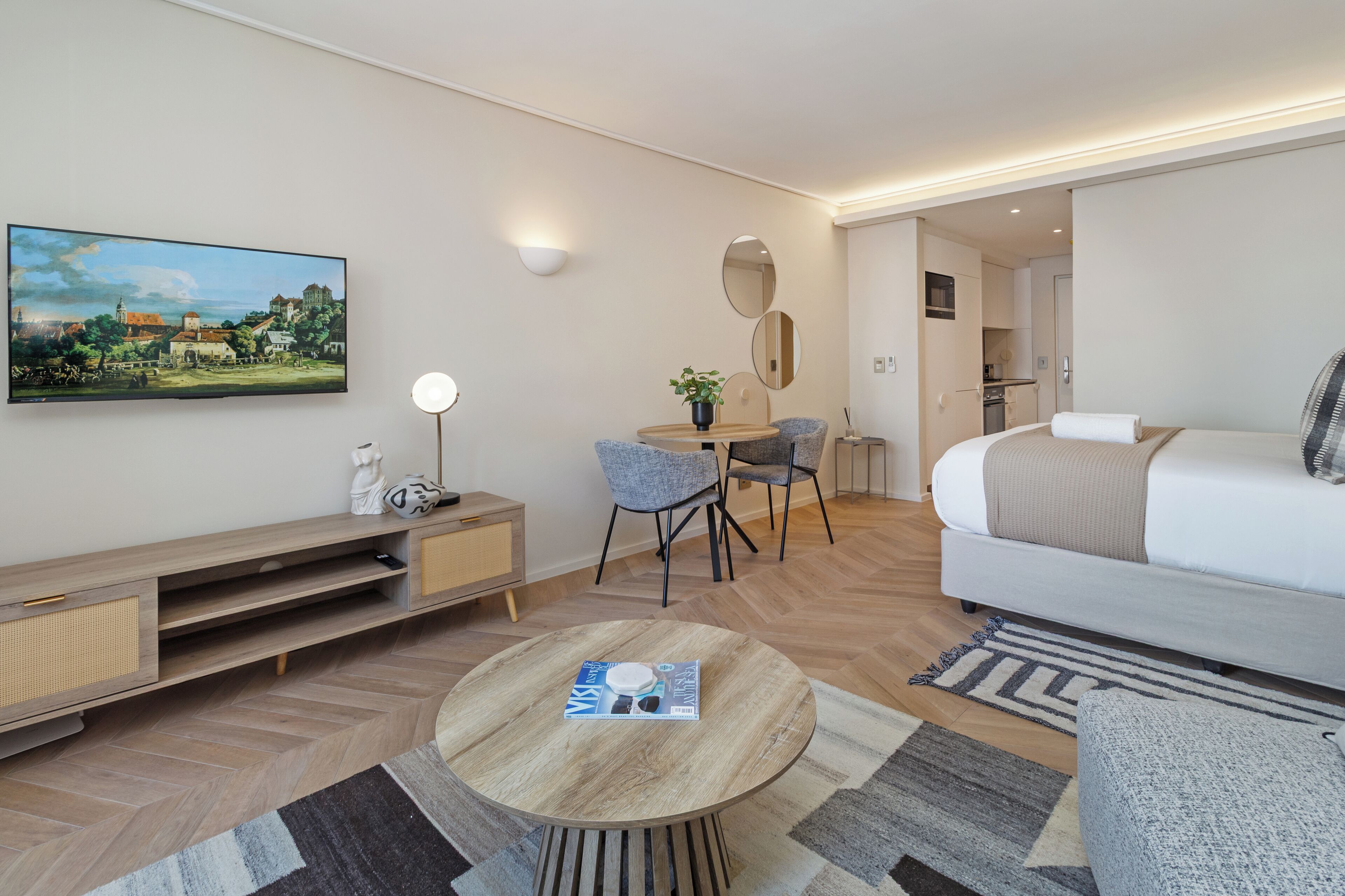 Une chambre d’hôtel moderne équipée d’un lit, d’une table à manger, d’un téléviseur et d’un coin salon avec des fauteuils.