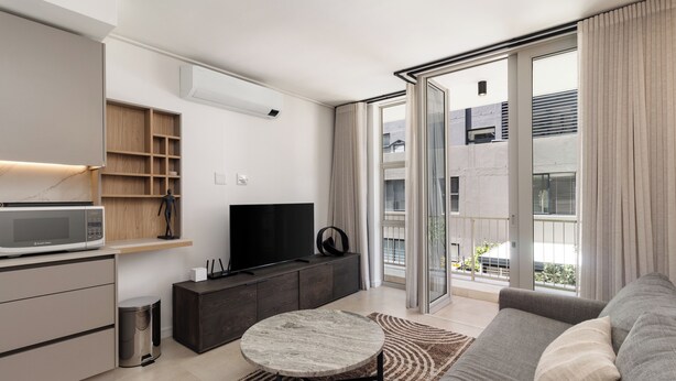 Een moderne woonkamer met een bank, een salontafel, een televisie en een schuifdeur naar een balkon.
