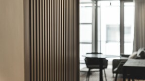 Een modern interieur met een hoge, gestreepte zuil, een eethoek met tafel en stoelen, en grote ramen die natuurlijk licht binnenlaten.