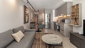 Een moderne woonkamer met een grijze bank, een ronde salontafel en een eethoek met stoelen.