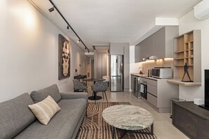 A modern living room with a grey sofa, a round coffee table, and a dining area with chairs. - Trendy Green Point Apartment | Central Location (Cape Town)