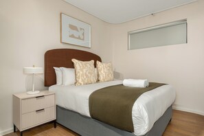A neatly made bed with a brown headboard, a bedside table with a lamp, and patterned pillows. - Dolce Vita | Sleek Apartment (Cape Town)