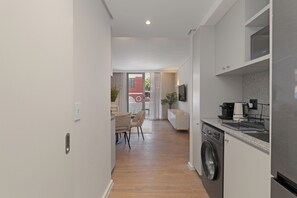 Une cuisine moderne équipée d’un lave-linge, un coin repas avec une table et des chaises, et une vue sur un immeuble rouge, visible à travers la porte vitrée.