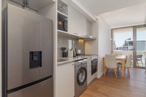 A modern kitchen with stainless steel appliances, a built-in washing machine, and a dining area with a view. - Dolce Vita | Sleek Apartment Near Promenade (Cape Town)