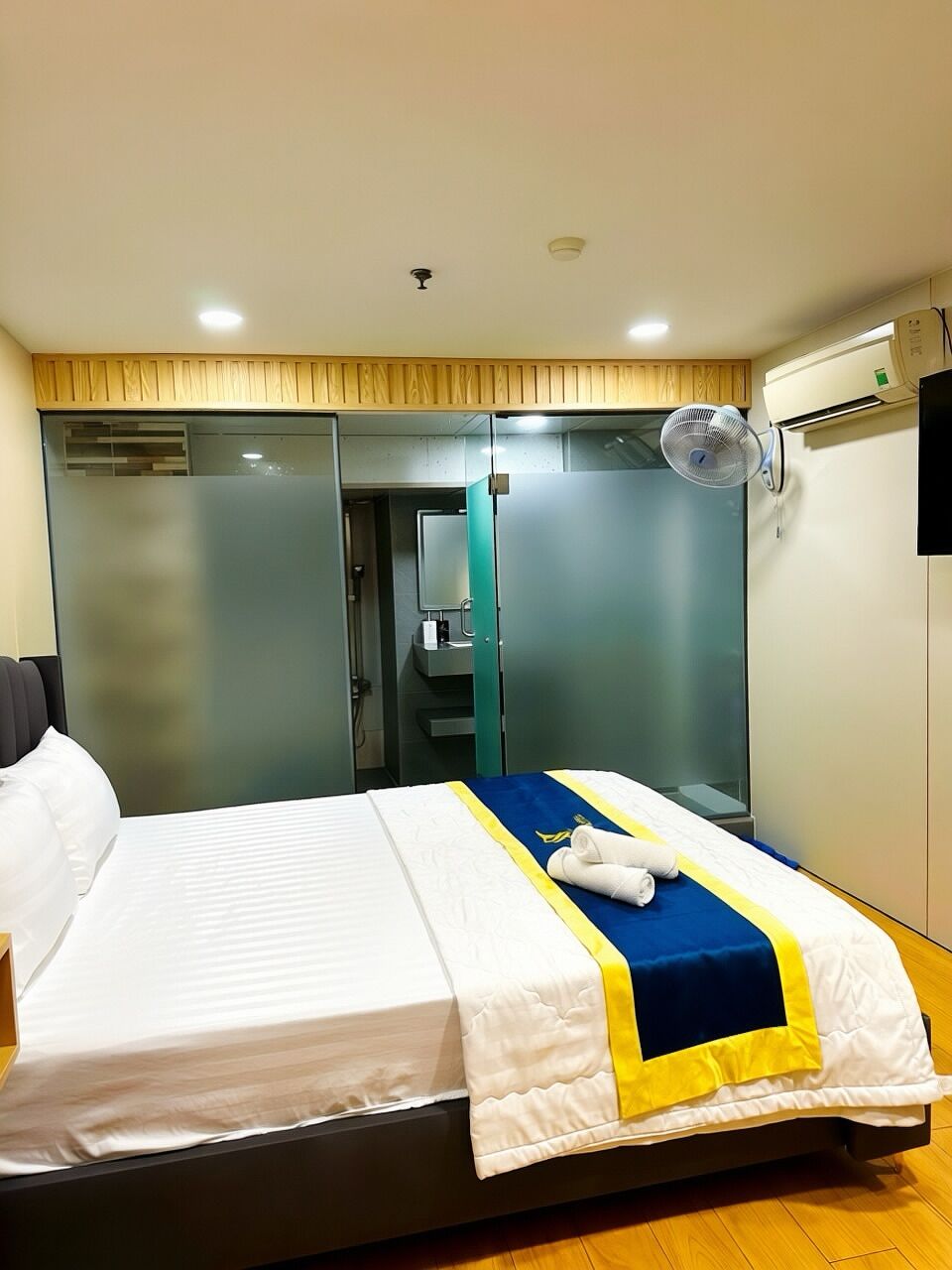 A hotel room with a bed, a mirror, a fan, and a window.