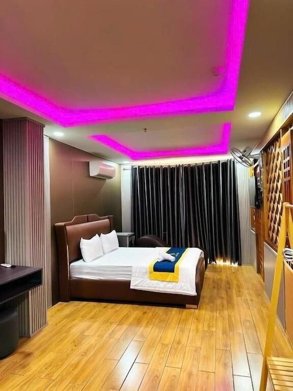 Una habitación de hotel moderna con una cama, suelo de madera, un escritorio y un armario.