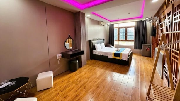 A modern bedroom with a bed, bedside table, and a small seating area. - Kim Linh Hotel  (Ho Chi Minh City)