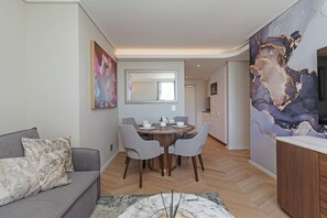 A modern living room with a grey sofa, a round dining table with four chairs, a large mirror, and a marble coffee table. - Dolce Vita | Prime Sea Point Location (Cape Town)
