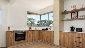 Une cuisine moderne avec des meubles en bois, un four encastré et une fenêtre donnant sur les arbres.
