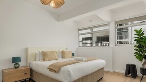 Une chambre moderne avec un grand lit, une table de chevet, une lampe, une fenêtre donnant sur un beau paysage et une plante en pot.