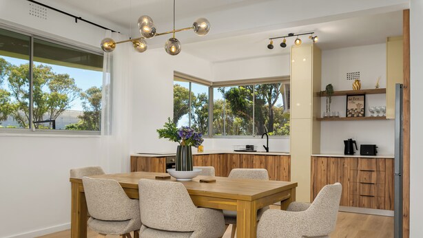 Un espace de restauration moderne avec une table et des chaises en bois, un vase rempli de fleurs et une vue sur les arbres à travers de grandes fenêtres.