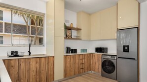 Une cuisine moderne avec des meubles en bois, un réfrigérateur en acier inoxydable, un lave-linge et une fenêtre donnant sur un immeuble.