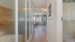 Un couloir avec une cloison en verre, un plancher en bois, une chaise et une porte donnant sur une salle de bain.