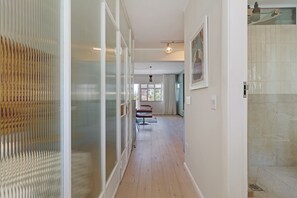 Ein Korridor mit Glastrennwand, Holzboden, einem Stuhl und einer Tür zu einem Badezimmer.